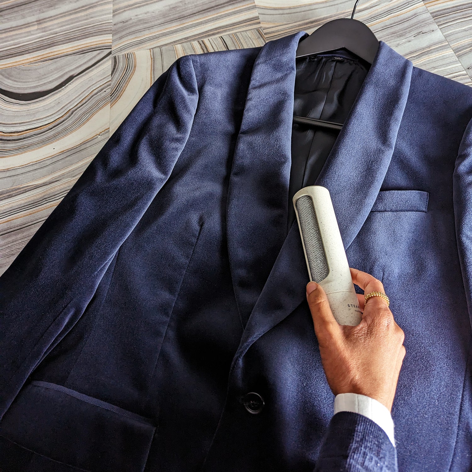 A hand holds up a sleek lint removing tool up to a navy blue velvet suit jacket