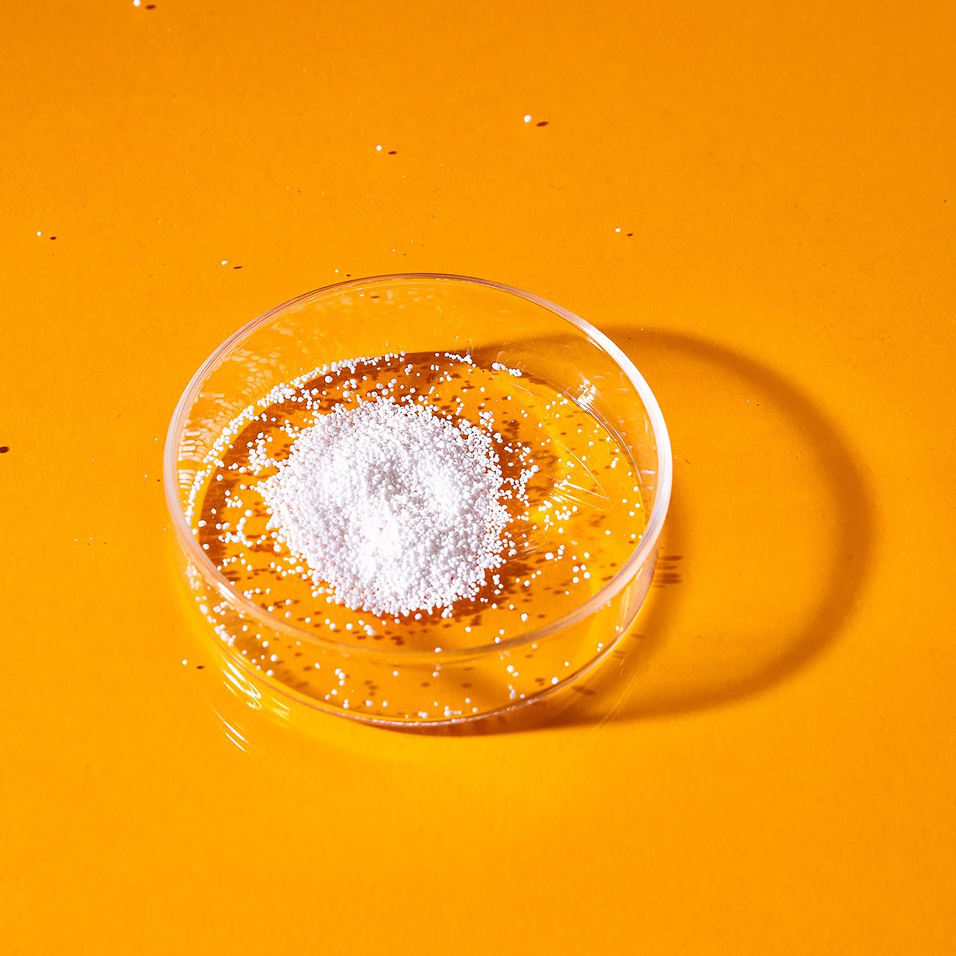 A single dose of white Supersalt oxygen booster powder is displayed in a petri dish on an orange background