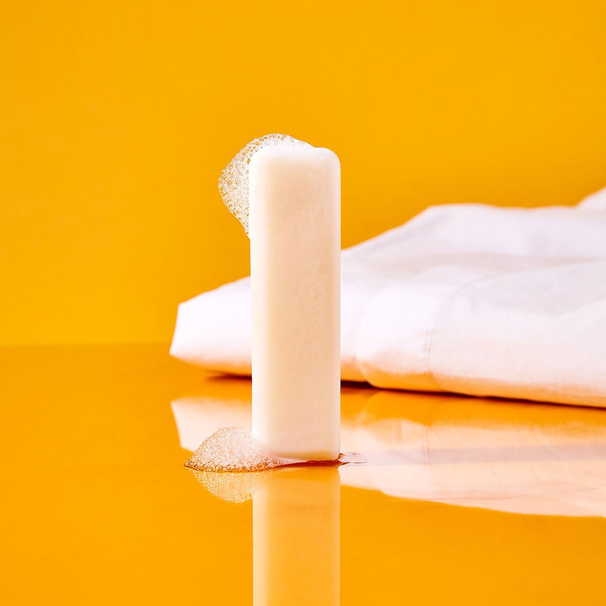 A sudsy soap stick displayed with white linens on an orange backdrop