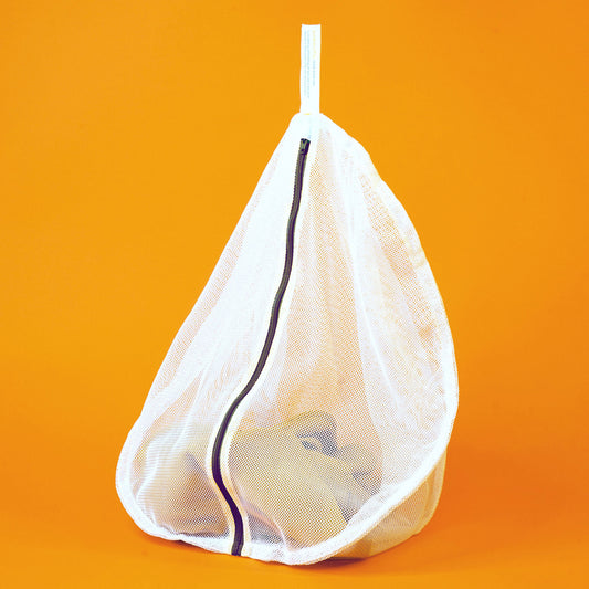 White mesh delicates bag by Soak with a charcoal zipper displayed on an orange backdrop; a piece of soft khaki clothing is visible inside