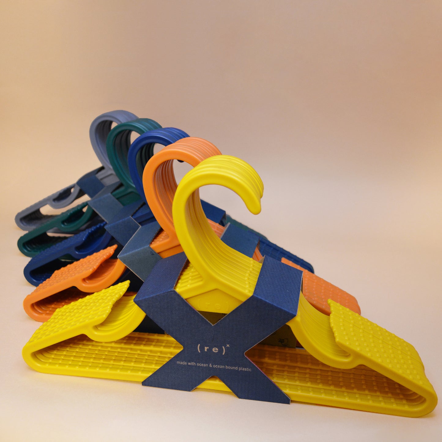 Five 10-packs of recycled ocean plastic hangers  (yellow, orange, blue, pine green and grey) held together by cardboard X-shaped labels