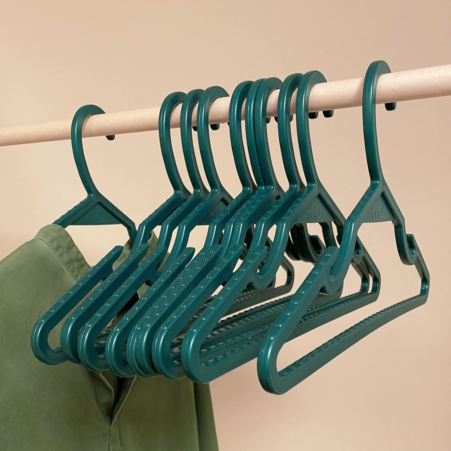Pine green recycled ocean plastic hangers on a wooden pole; a seaweed green tunic hangs from one of the hangers
