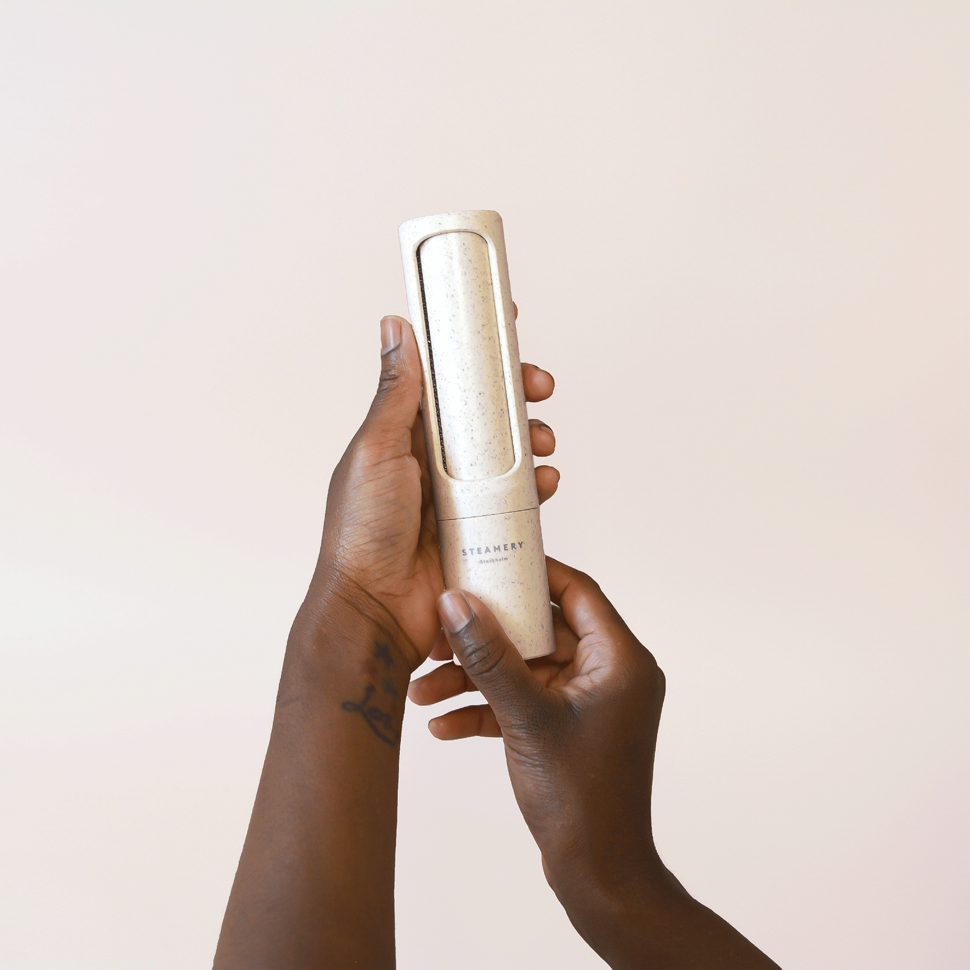 A gif of hands twisting open a beige speckled reusable lint roller in front of a beige backdrop