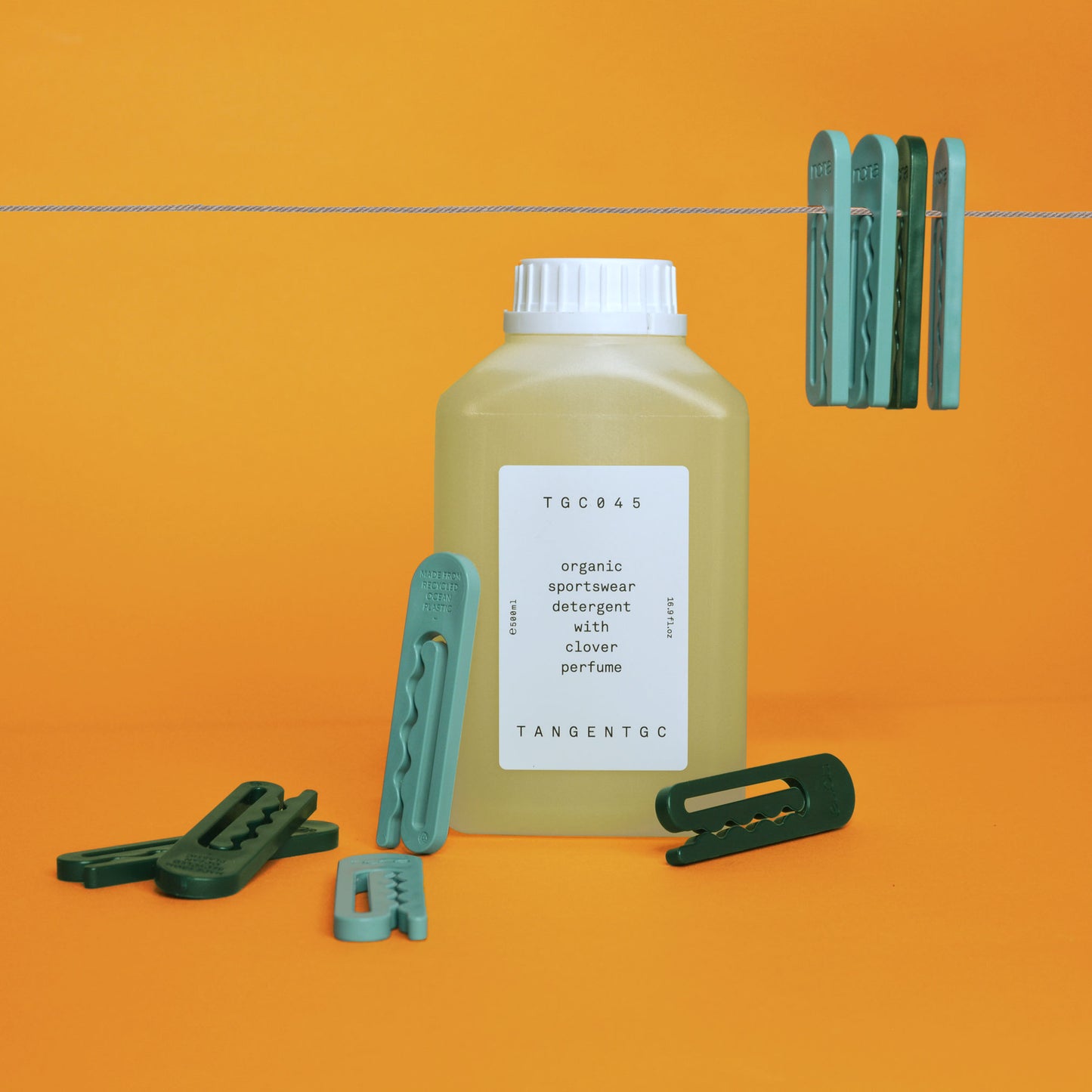 A bottle of sportswear specialty detergent photographed with green ocean plastic clothespins, some of which hang from a clothesline overhead
