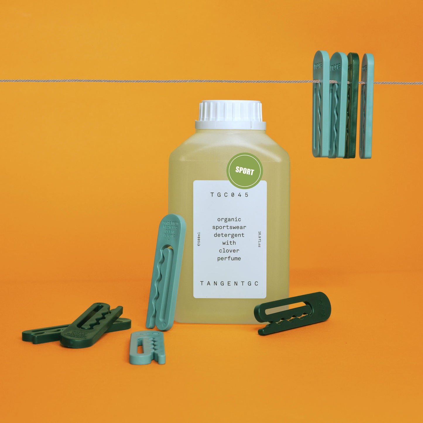 A bottle of sportswear specialty detergent photographed with recycled ocean plastic clothespins, some of which hang from a clothesline overhead