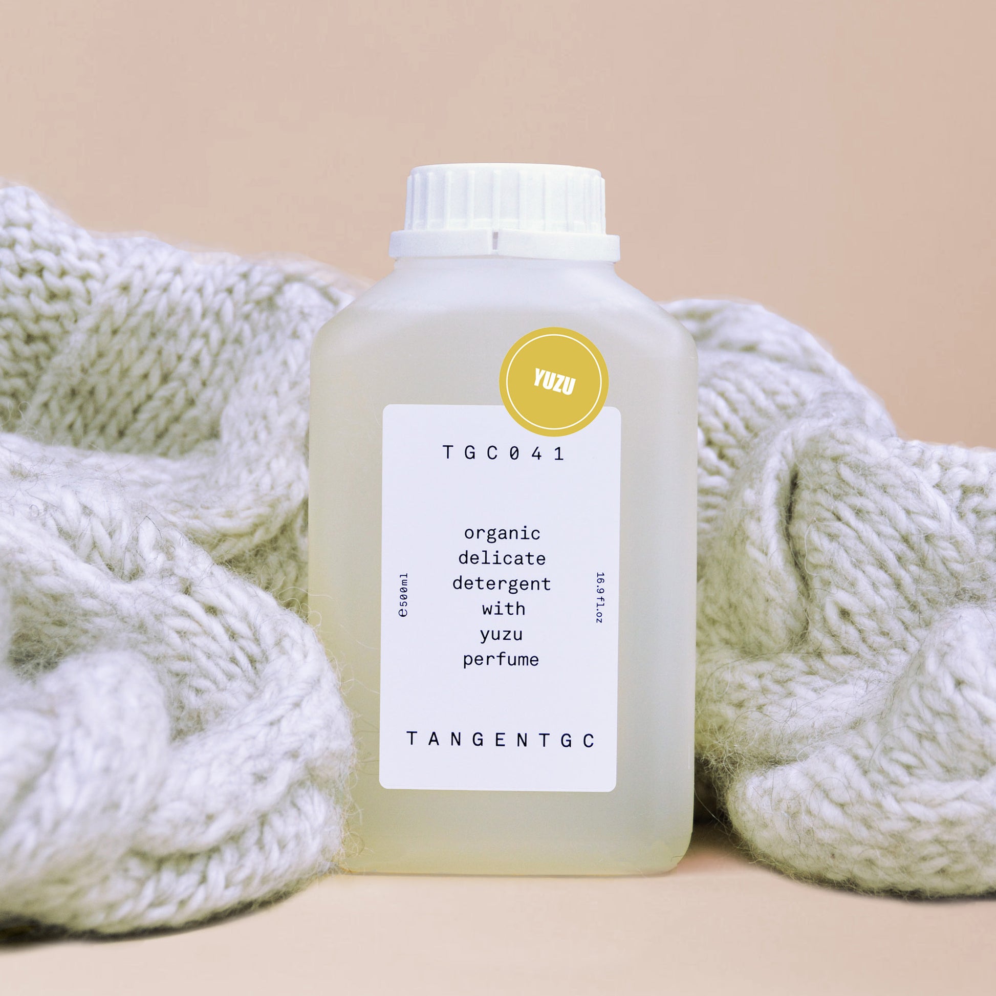 A  cream colored chunky wool sweater wrapped around a rectangular bottle of yuzu delicate detergent by Swedish brand Tangent Garment Care
